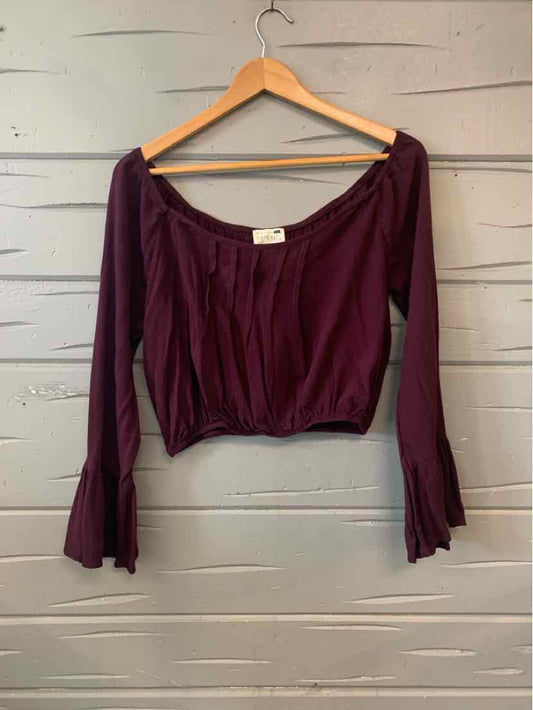 Purple off-shoulder long sleeve top with flared cuffs on wooden hanger against gray wooden background.