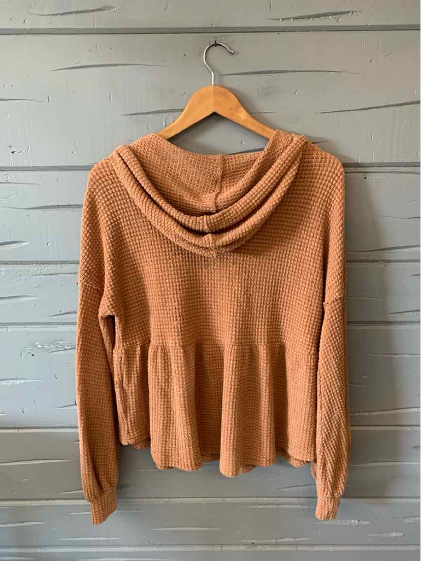 Tan knit hooded sweater with long sleeves and a peplum hem hanging on a wooden hanger.