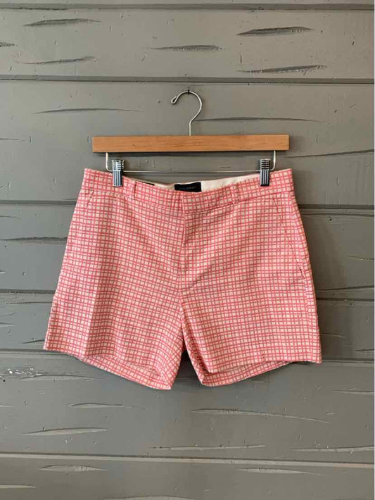 Pink and white checkered cotton shorts with front pockets and zipper closure hanging on wooden hanger.