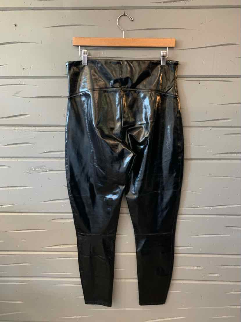 Black shiny Spanx high-waisted leggings with a smooth finish, hanging from a clip hanger.