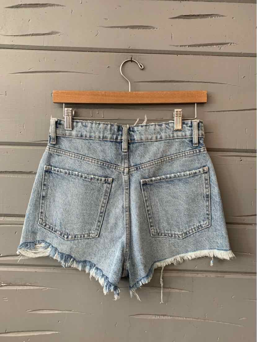 Light wash denim shorts with frayed hems and two back pockets on a wooden hanger.