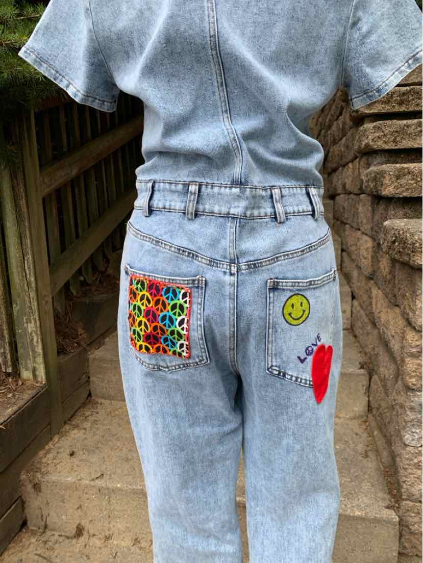 Light blue denim jeans with colorful patchwork and embroidered smiley face and heart on back pockets.