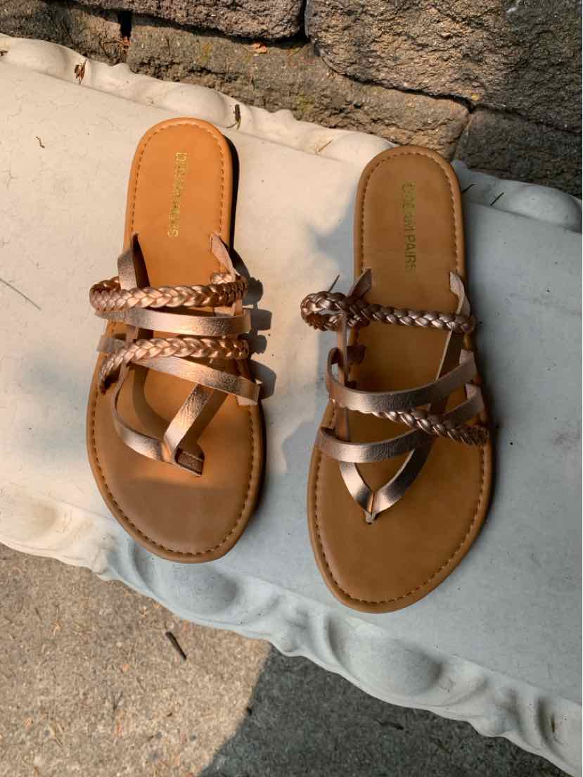 Rose gold flat sandals with braided and smooth leather straps, open-toe design, and tan footbed.