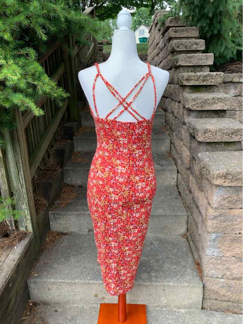Red floral midi dress with thin crisscross straps and fitted silhouette on mannequin outdoors.