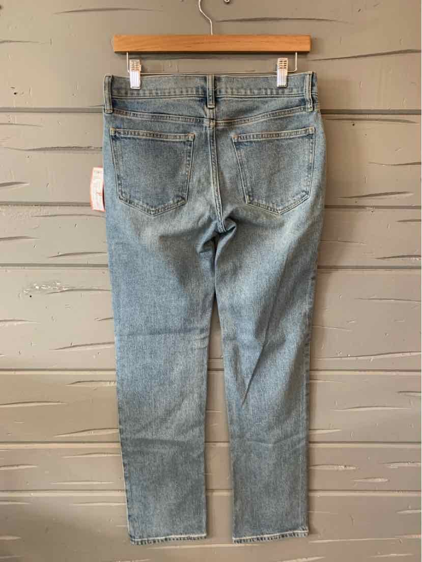 Light blue denim jeans with a straight-leg cut and classic five-pocket design hanging on a wooden hanger against a pale gray