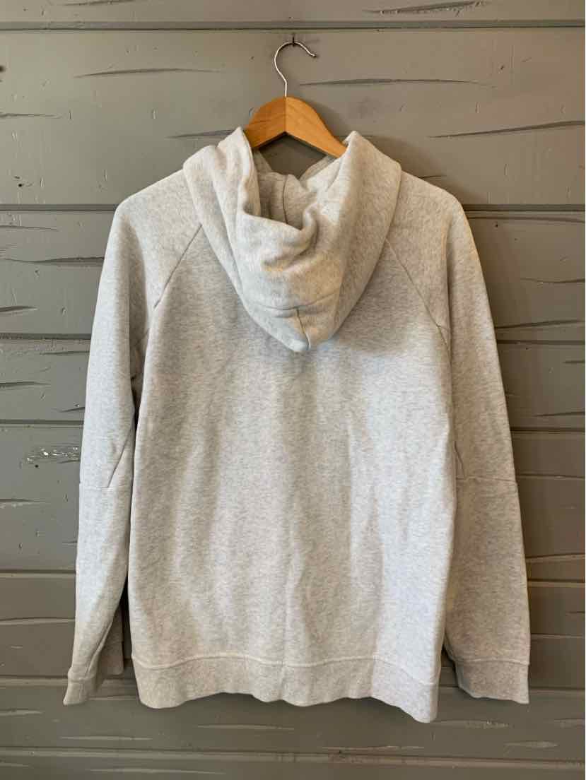 Light gray hoodie with long sleeves and a relaxed fit hanging on a wooden hanger against a gray wooden wall.