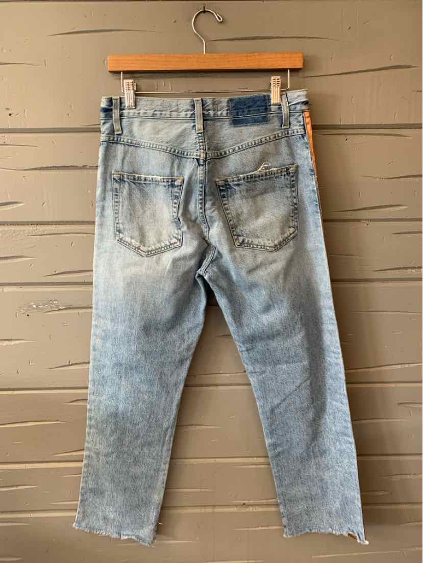Light wash denim jeans with frayed hems and back patch pockets hanging on wooden hanger.