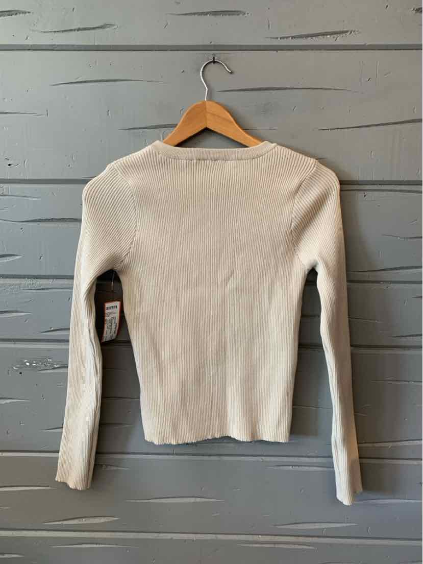Beige ribbed long-sleeve sweater with crew neckline and fitted silhouette hanging on wooden hanger.