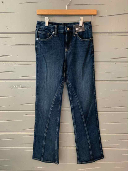 Dark blue slim-fit denim jeans with front pockets and button closure hanging on wooden hanger against gray wall.