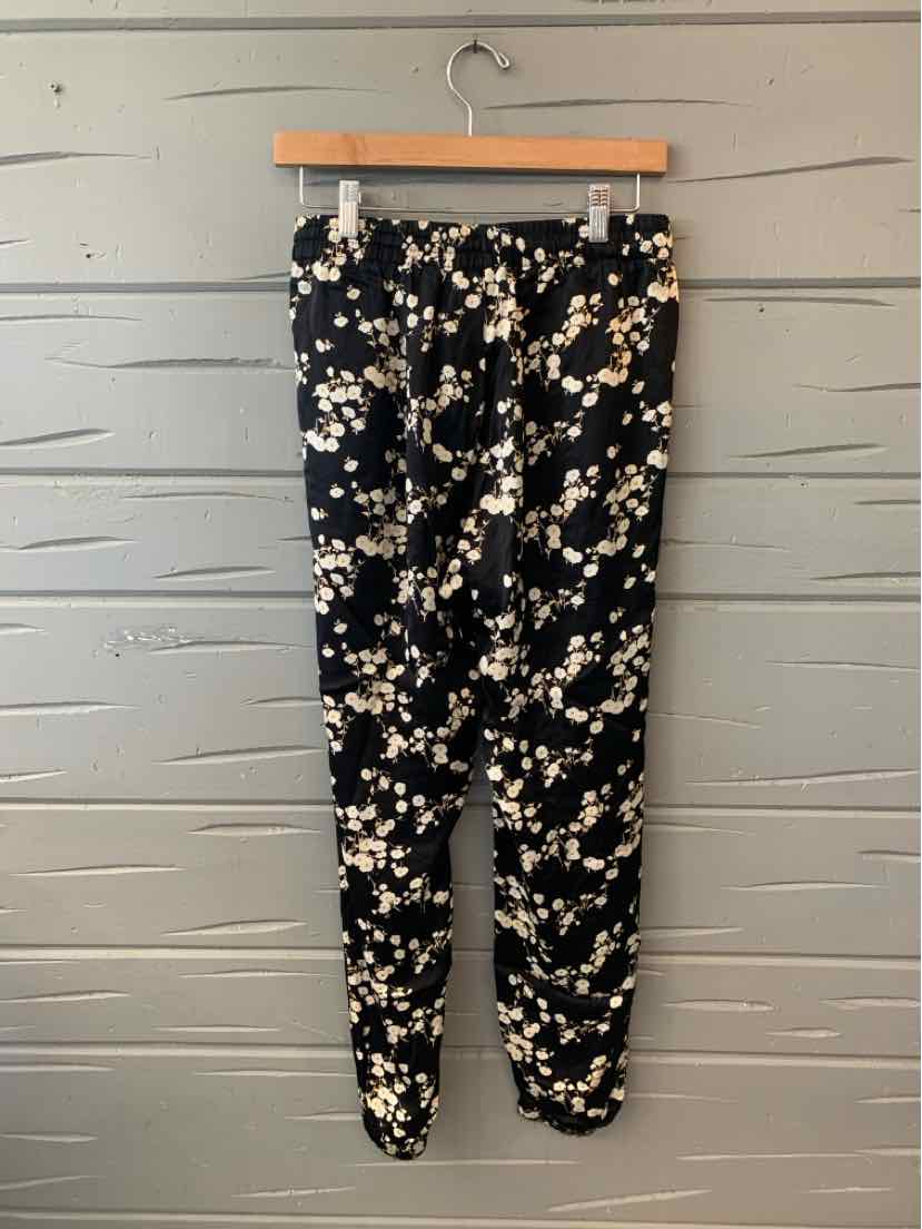 Black tapered pants with white floral print, elastic waistband, and cuffed ankles.