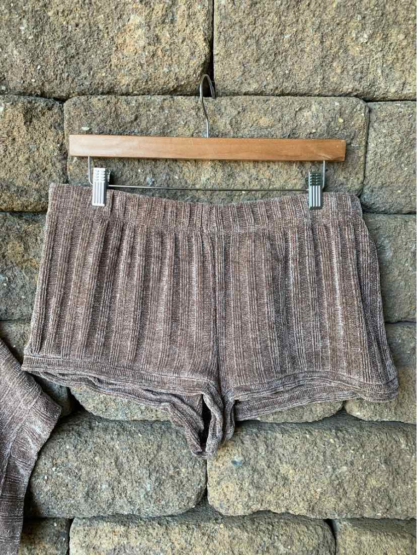 Brown chenille knit shorts with elastic waistband hanging on wooden hanger against stone wall background.