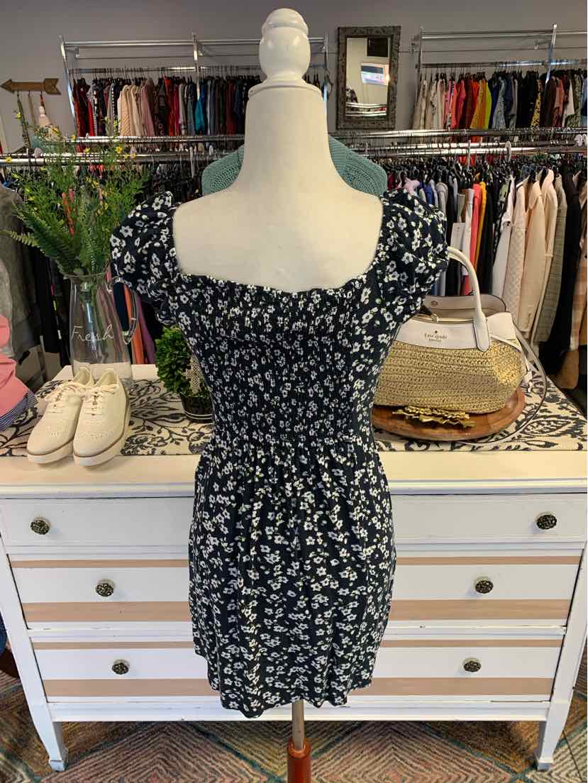Black mini dress with white floral print, square neckline, and puffed short sleeves.