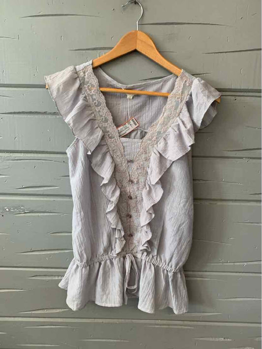 Light gray sleeveless blouse with ruffled V-neckline and peplum hem hanging on wooden hanger.
