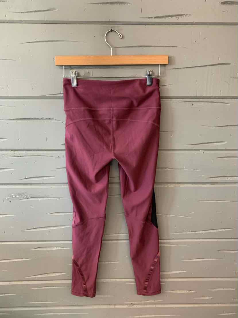 Mauve-colored Under Armour women's leggings with a high waist and fitted ankle cuffs hanging on a wooden hanger against a.