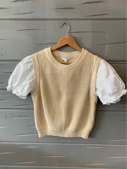 Beige knit sleeveless sweater layered over white puffed short sleeves blouse on wooden hanger.