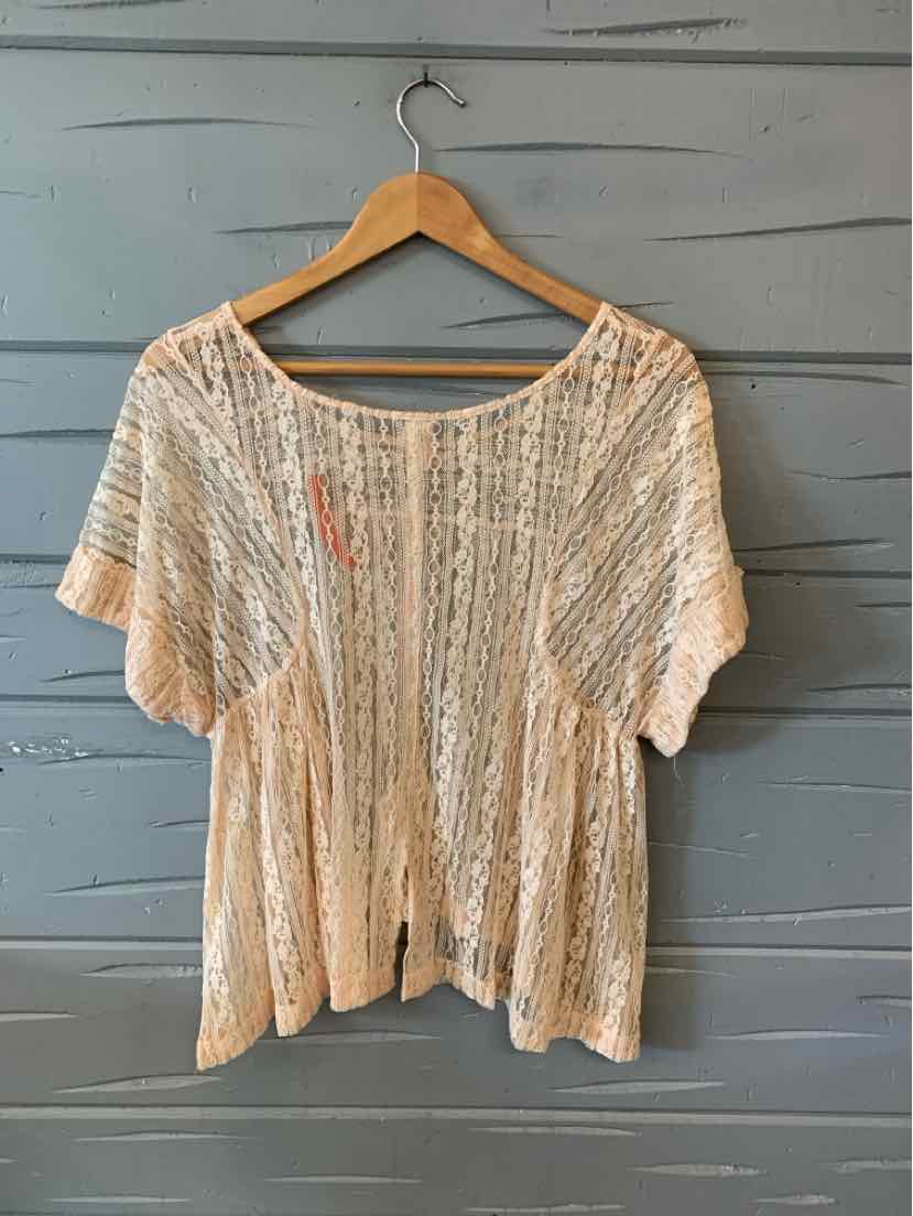 Nude lace short-sleeve blouse with loose fit and boat neckline on wooden hanger against gray wall.