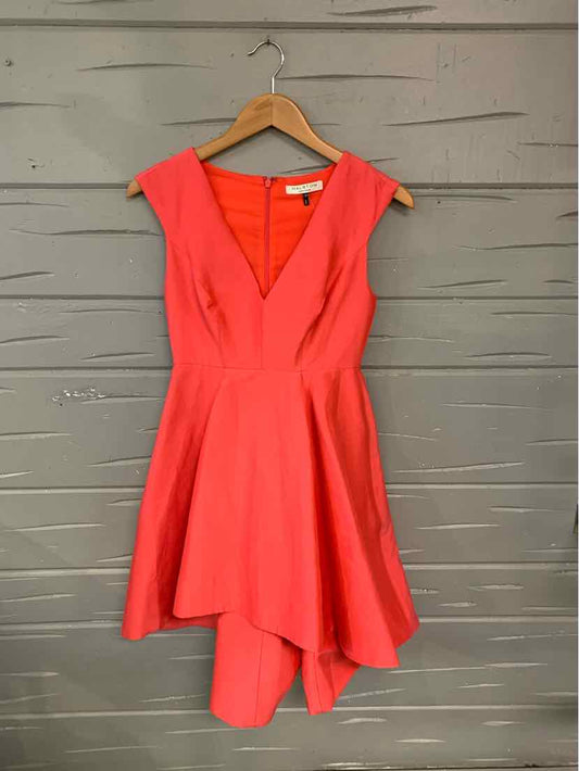 Coral pink sleeveless dress with deep V-neck and asymmetric hem on wooden hanger.