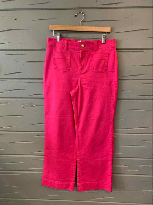 Bright pink cropped pants with front pockets and button closure hanging on wooden hanger.