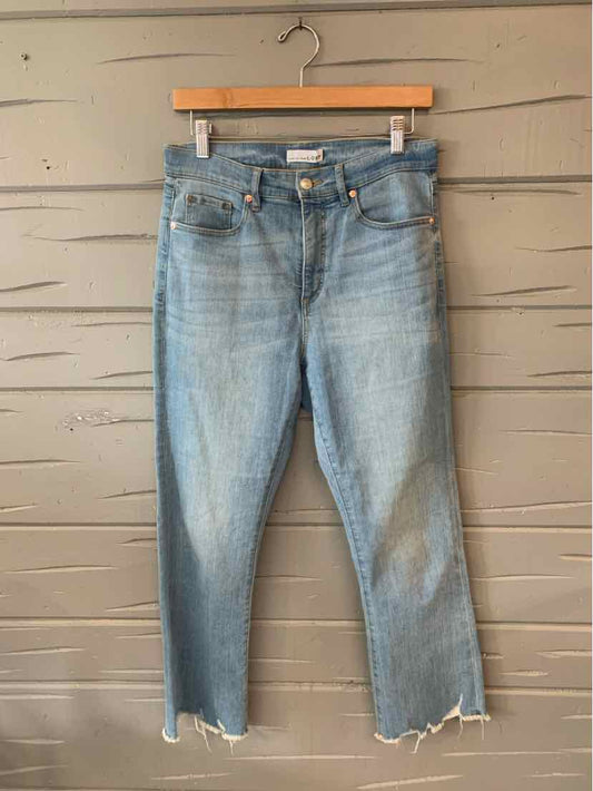 Light wash blue denim jeans with frayed hems and classic five-pocket design hanging on wooden hanger.