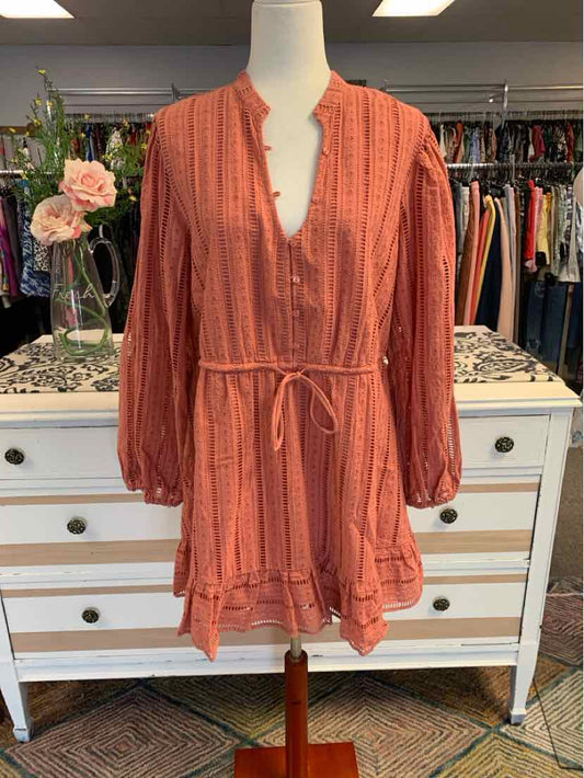 Coral orange long-sleeve romper with V-neck, button front, cinched waist tie, and ruffle hem.