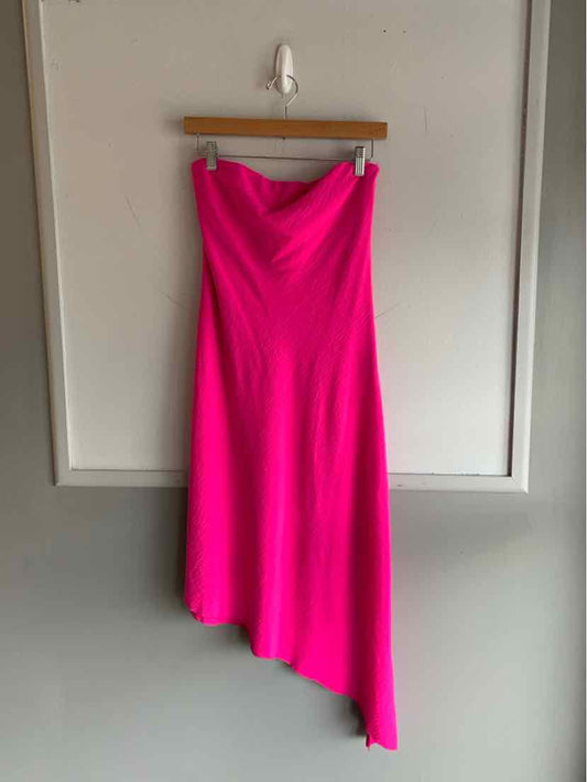 Bright pink sleeveless dress with an asymmetrical hem and fitted bodice hanging on wooden hanger.