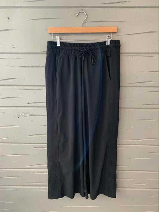 Black wide-leg pants with drawstring waist and side pockets hanging on wooden hanger.