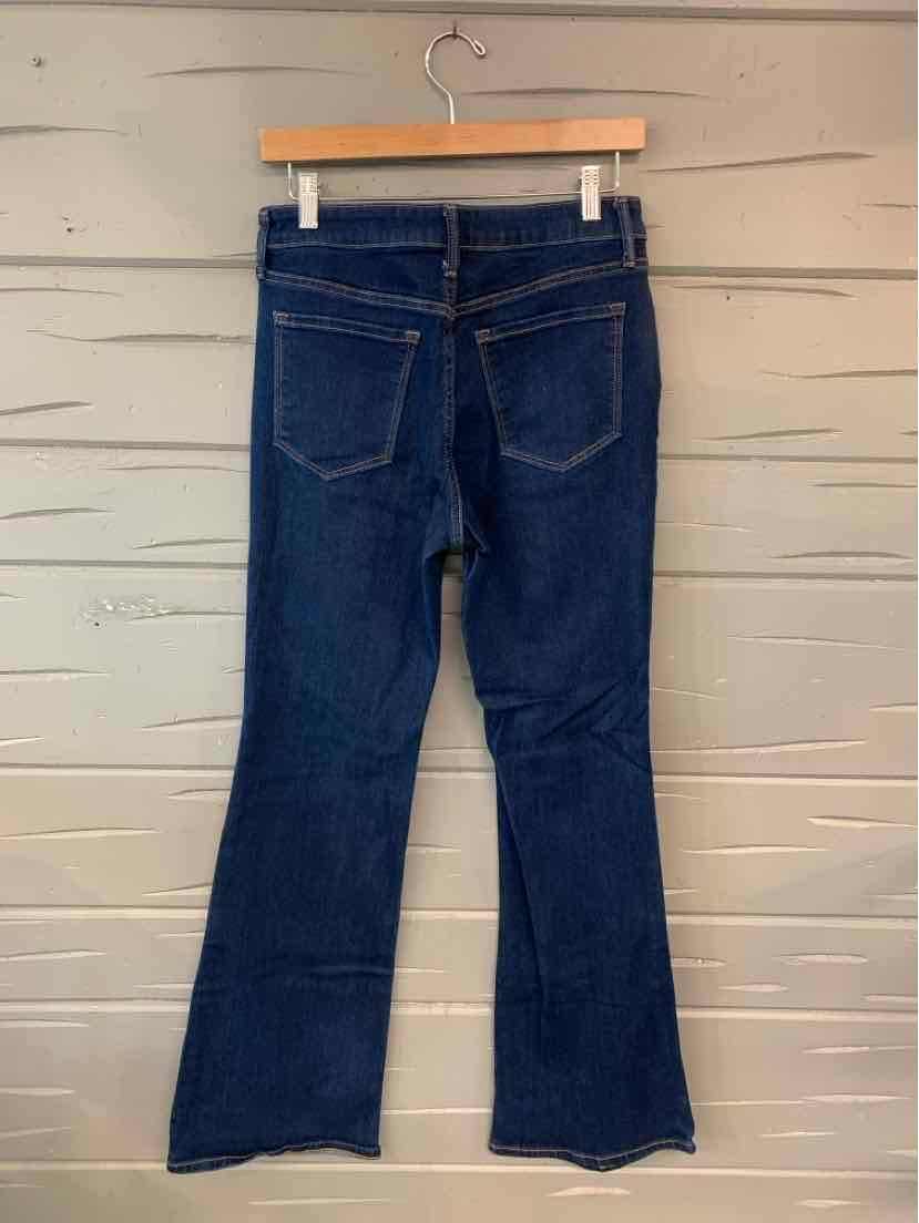 Dark blue denim bootcut jeans with back pockets and belt loops on wooden hanger against gray wall.