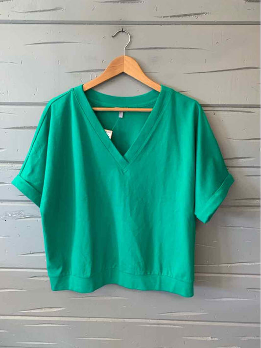 Green short-sleeve blouse with V-neck and relaxed fit on wooden hanger.