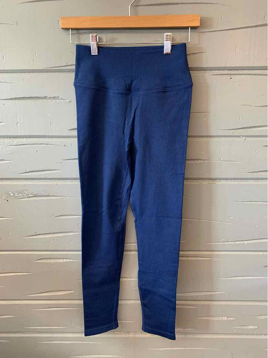 Navy blue ribbed high-waist leggings hanging on wooden hanger against white textured wall.