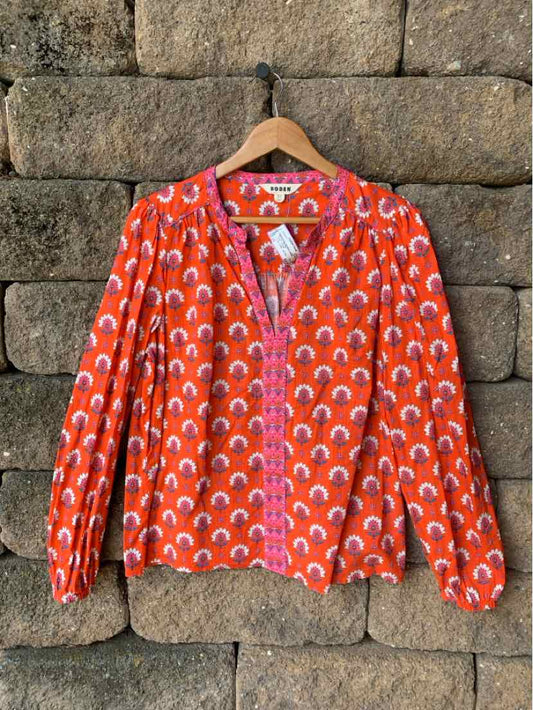 Long-sleeve orange blouse with white and pink floral semi-circle pattern, round neckline, and buttoned front.