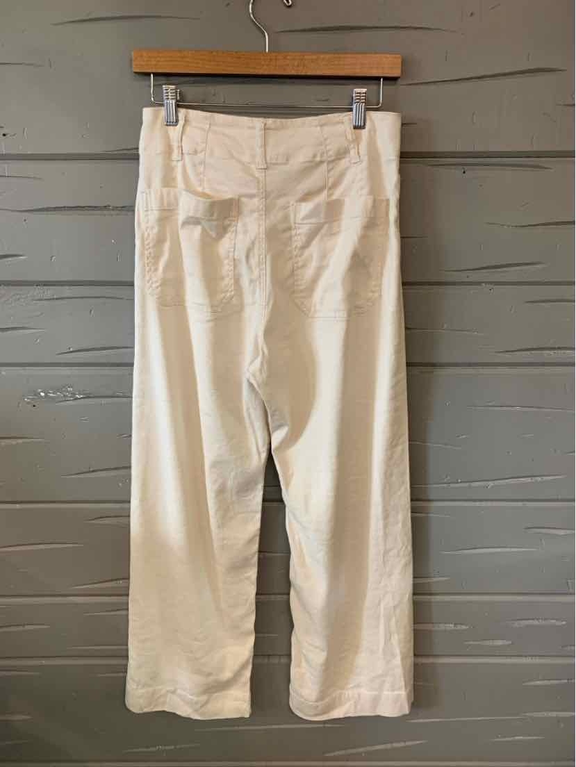 High-waisted cream pants with a straight-leg fit and front seam detailing hanging on wooden hanger.