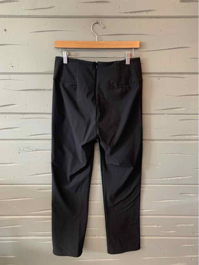 Black tailored pants hanging on wooden hanger against gray textured wall.