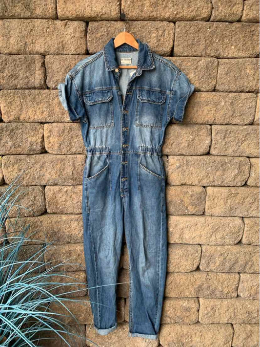 Blue denim jumpsuit with short sleeves, button-up front, chest and side pockets, and a cinched waist.