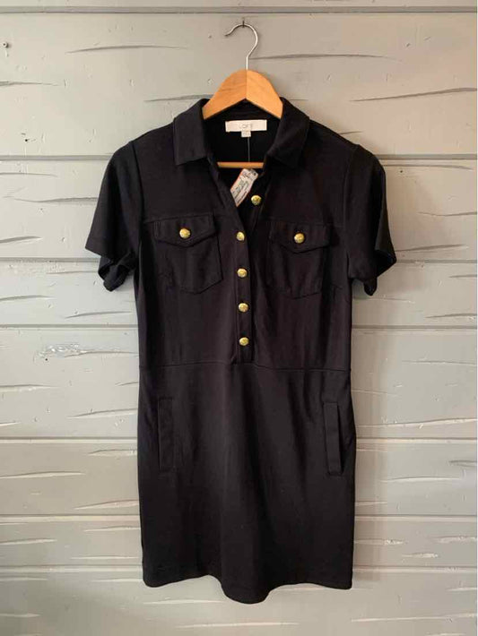 Black short-sleeve dress with button-up front and two chest pockets on wooden hanger.