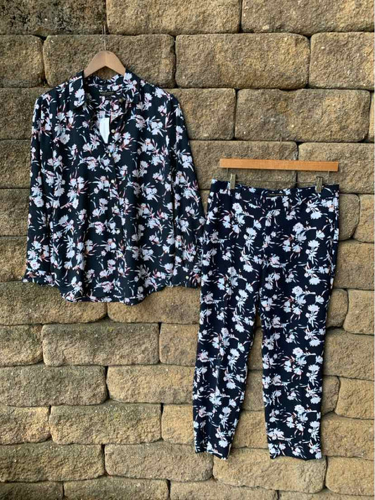 Black floral button-up blouse with matching tapered pants on wooden hangers against stone wall background.