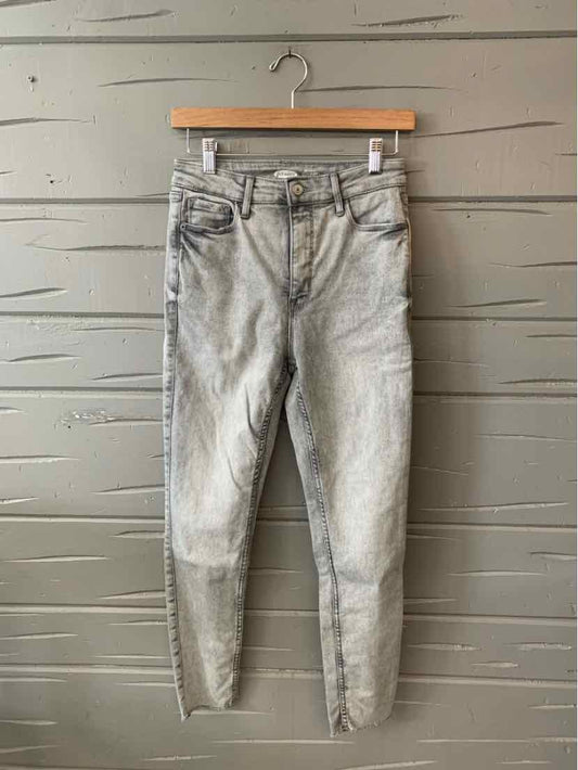 Gray washed denim jeans with five pockets and skinny fit hanging on wooden hanger against textured gray wall.