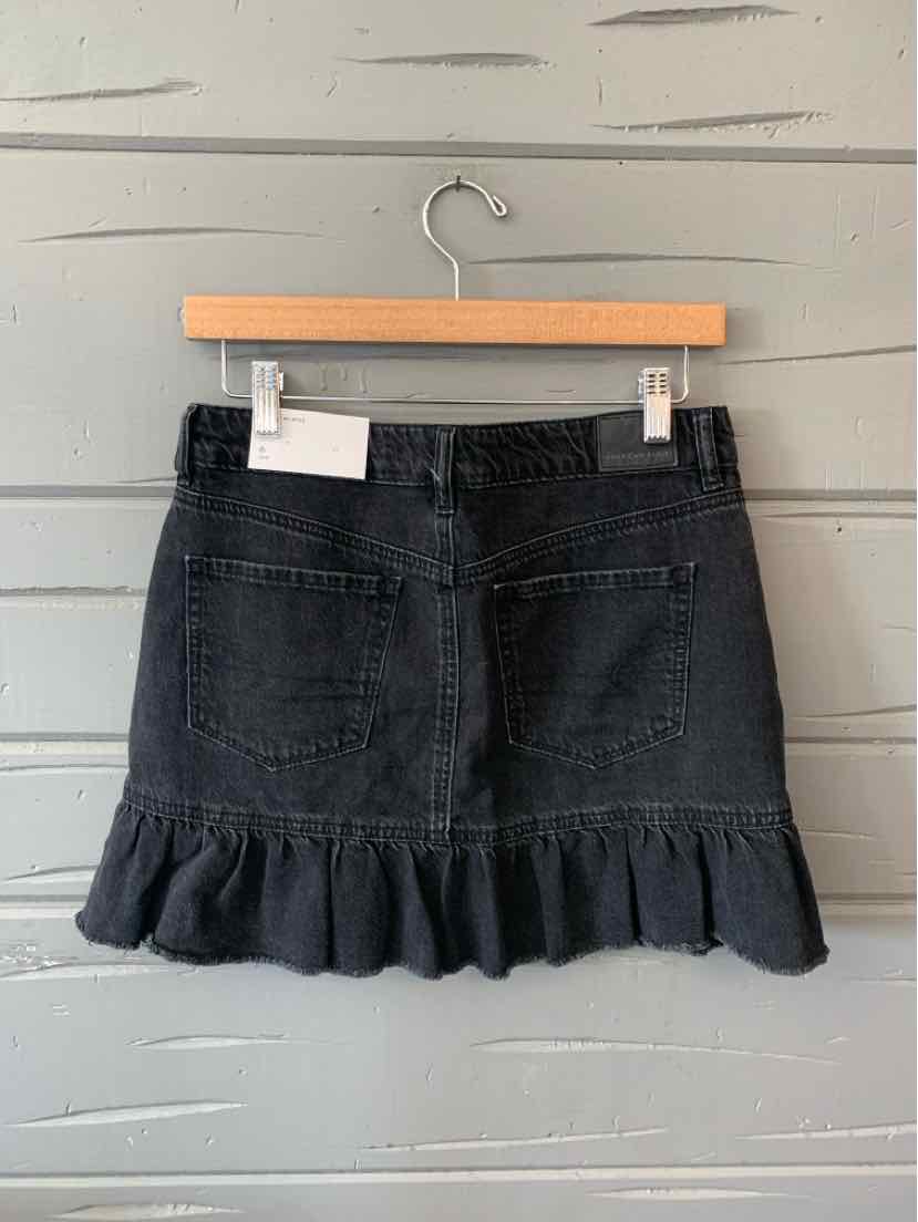 Black denim mini skirt with ruffled hem and back pockets hanging on wooden hanger.