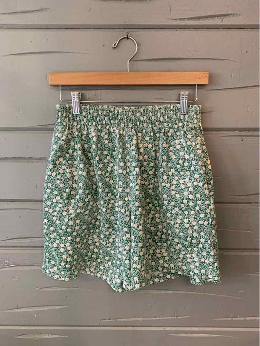 Green floral high-waist shorts with elastic waistband and loose fit hanging on wooden hanger.