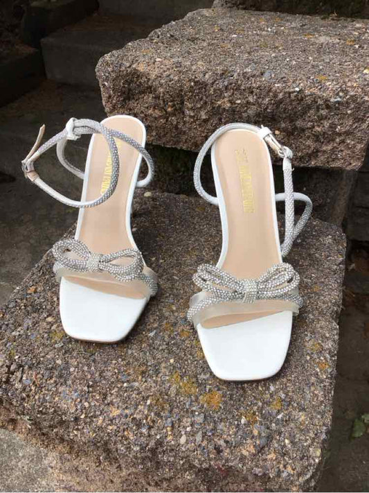 White strappy high-heeled sandals with square toes and braided front straps, ankle ties.