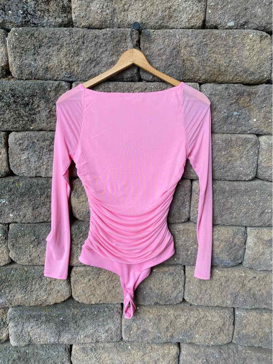 Pink long-sleeve ruched bodysuit with boat neckline and slim fit hanging on wooden hanger.
