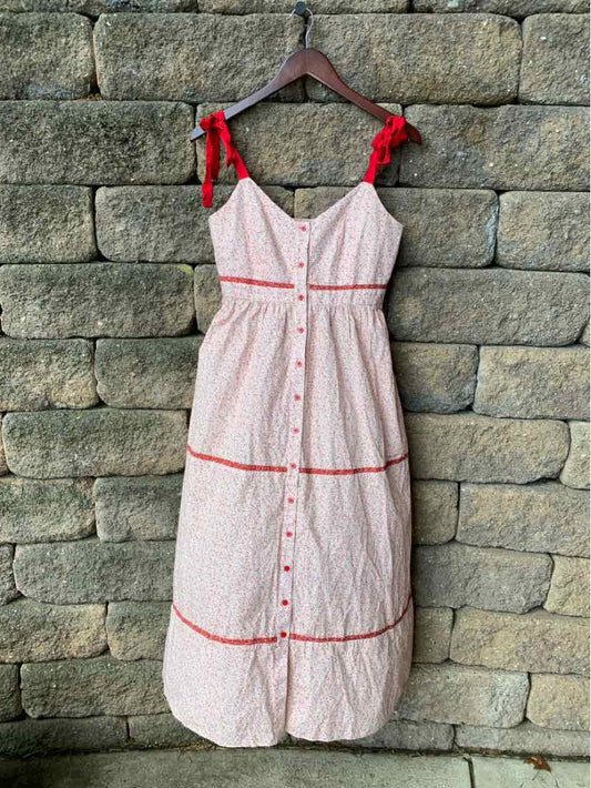 White midi dress with red floral print, red trim, button-down front, and tied shoulder straps.