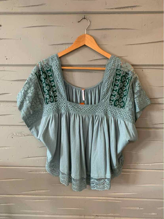 Light blue embroidered blouse with short sleeves and loose, flowy fit on wooden hanger.