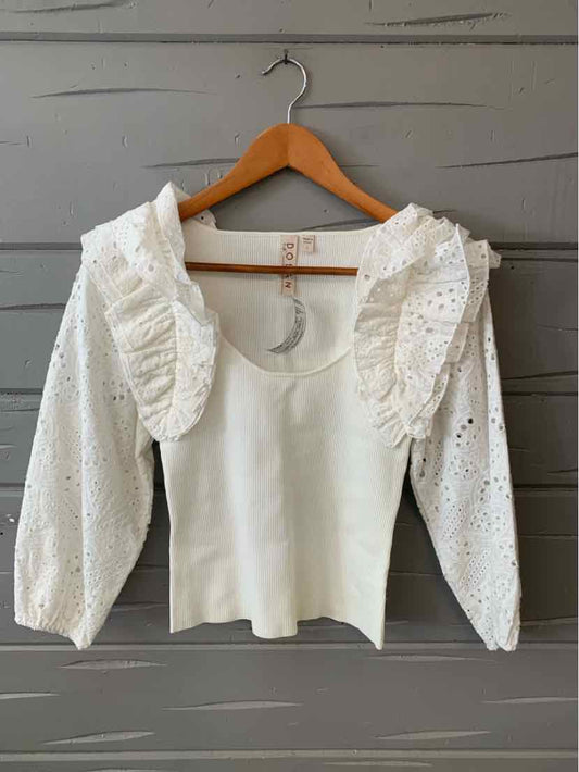 White eyelet blouse with large ruffled shoulder details and puffed long sleeves on wooden hanger.