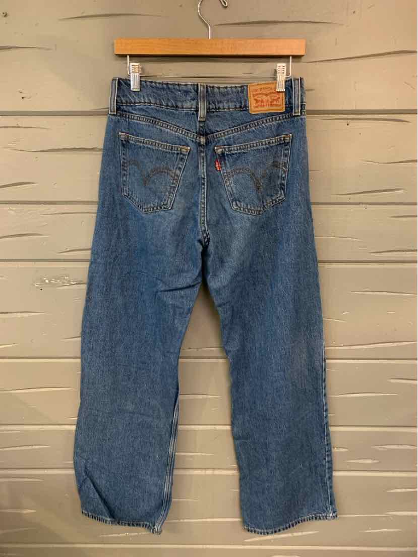 Blue high-waist Levi’s denim jeans with a straight leg and classic back pockets hanging on wooden hanger.