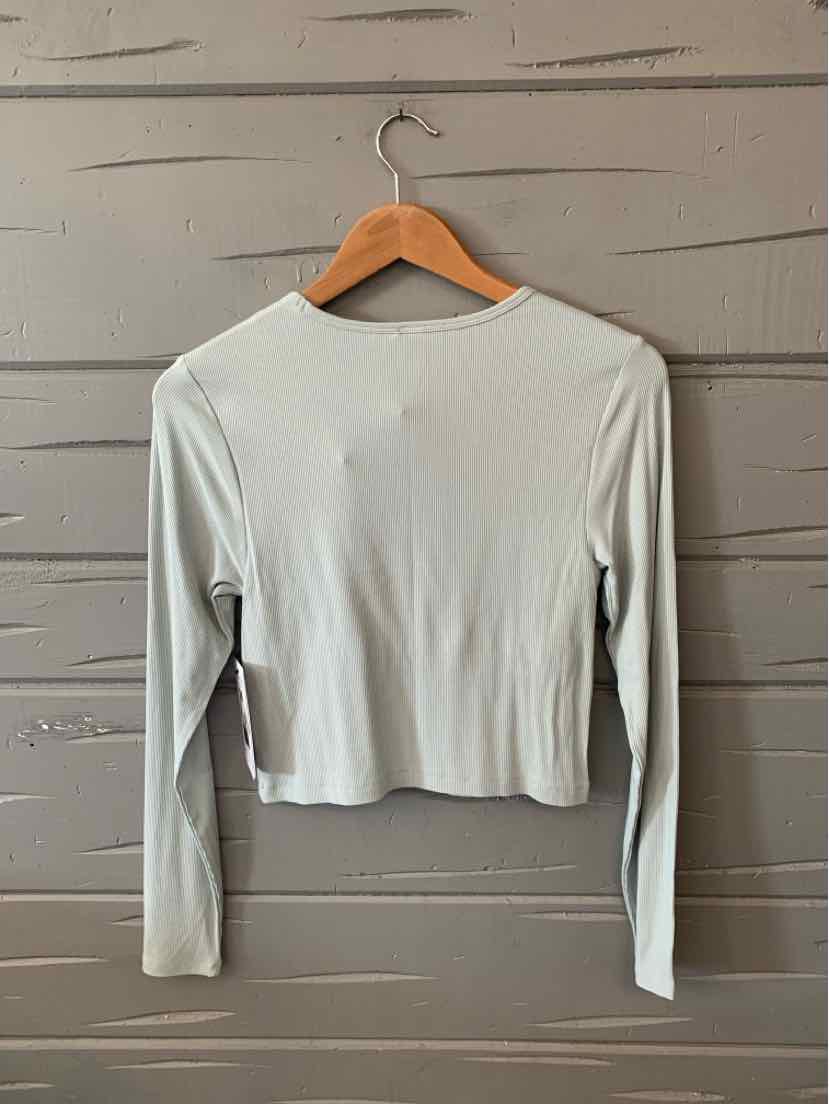 Light mint green ribbed long-sleeve crop top on wooden hanger against gray wood wall.