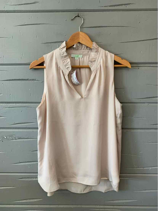 Sleeveless nude blouse with ruffled collar and V-neck on wooden hanger.