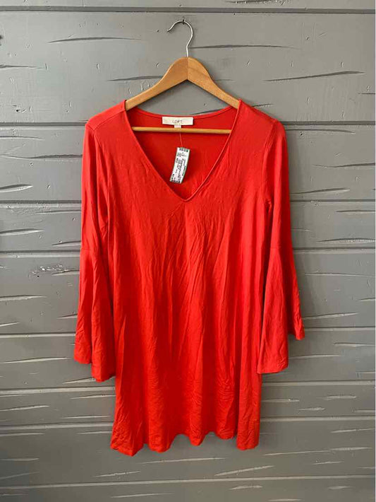 Bright red V-neck long sleeve dress with loose fit on wooden hanger against gray wall.
