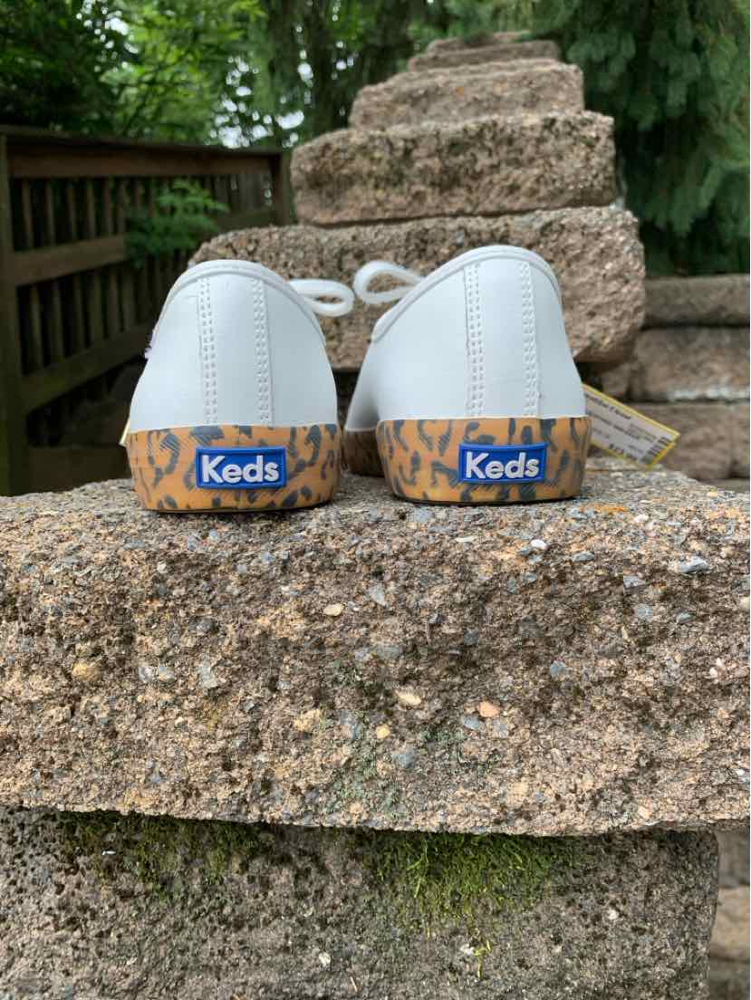 White low-top canvas sneakers with blue and orange Keds logo on the heel tab, size 8.
