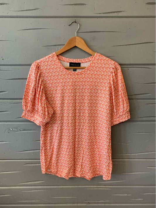 Orange floral-patterned blouse with puffed elbow-length sleeves on a wooden hanger.