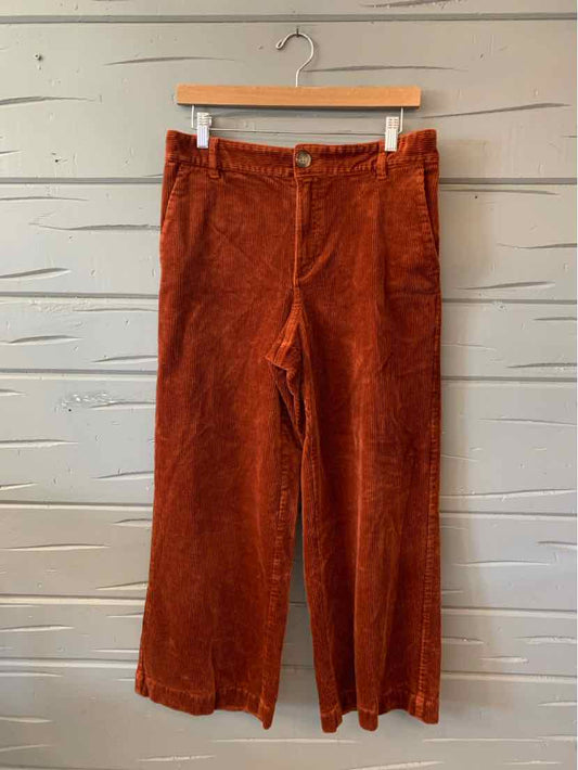 Rust-colored wide-leg corduroy pants with high waist and front pockets, hanging on wooden hanger.